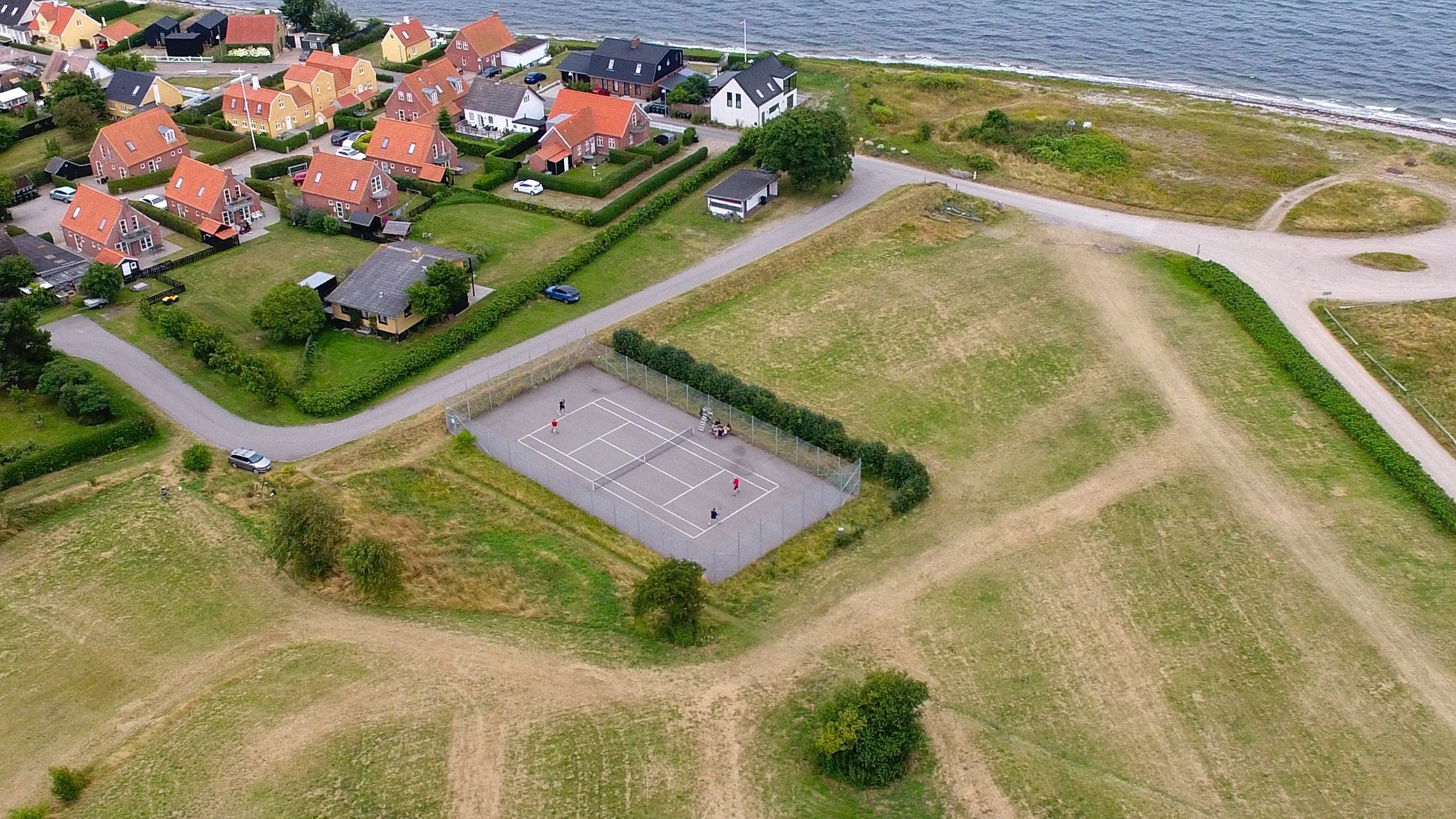 Luftfoto af tennisbanen ved Lohals Havn, med byen og kysten i baggrunden