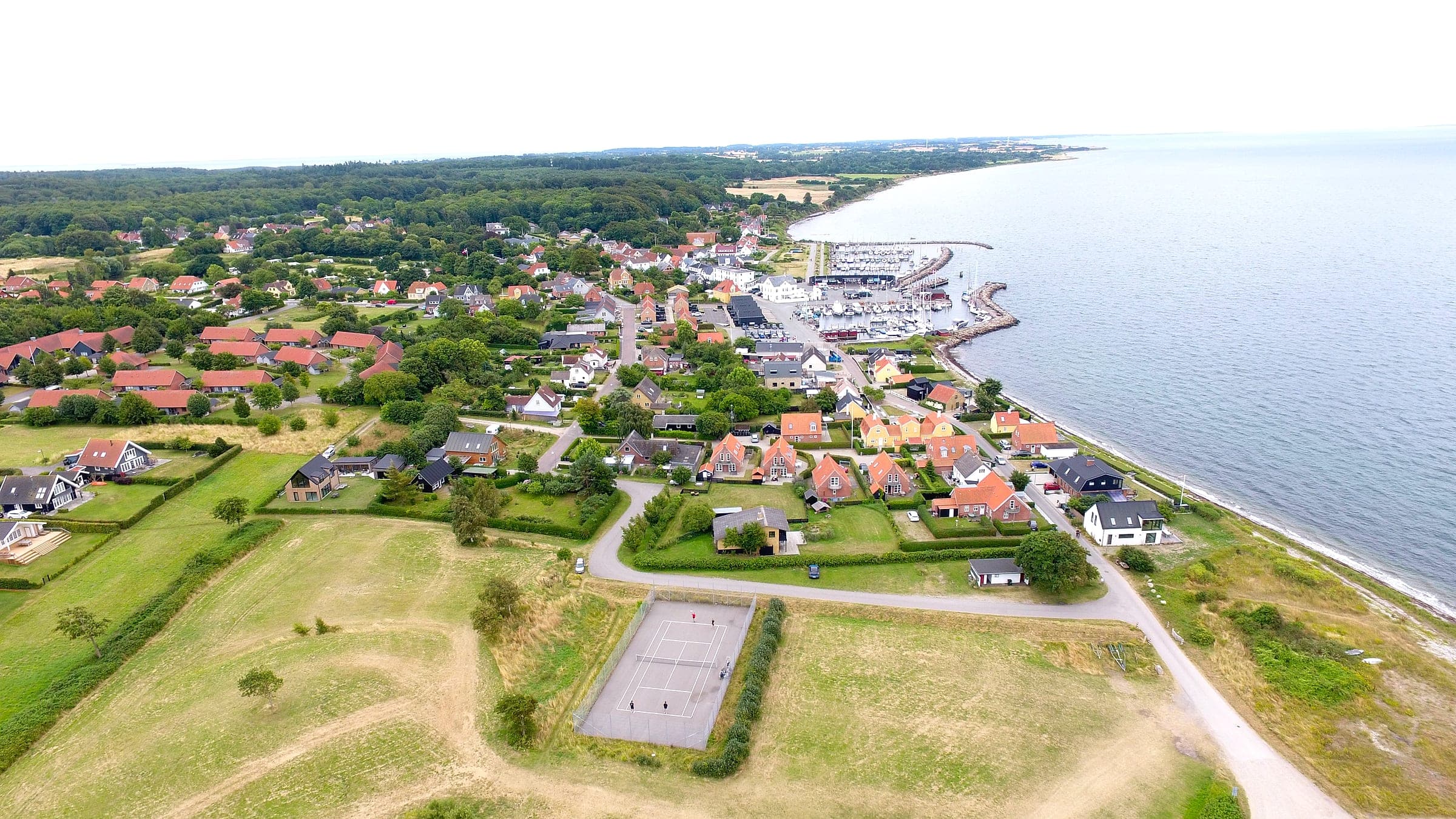 Luftfoto af Lohals med havnen, byen og tennisbanen i forgrunden