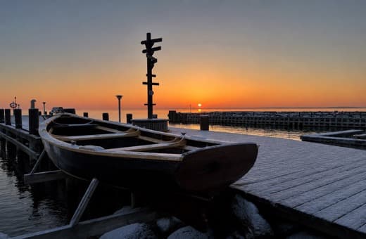 Snedækket robåd på broen ved havnen i solopgang