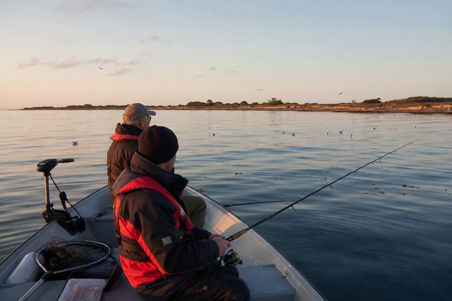 Bovmonteret elmotor på en mindre båd med to lystfiskere i redningsveste ved stille vande i aftenlys