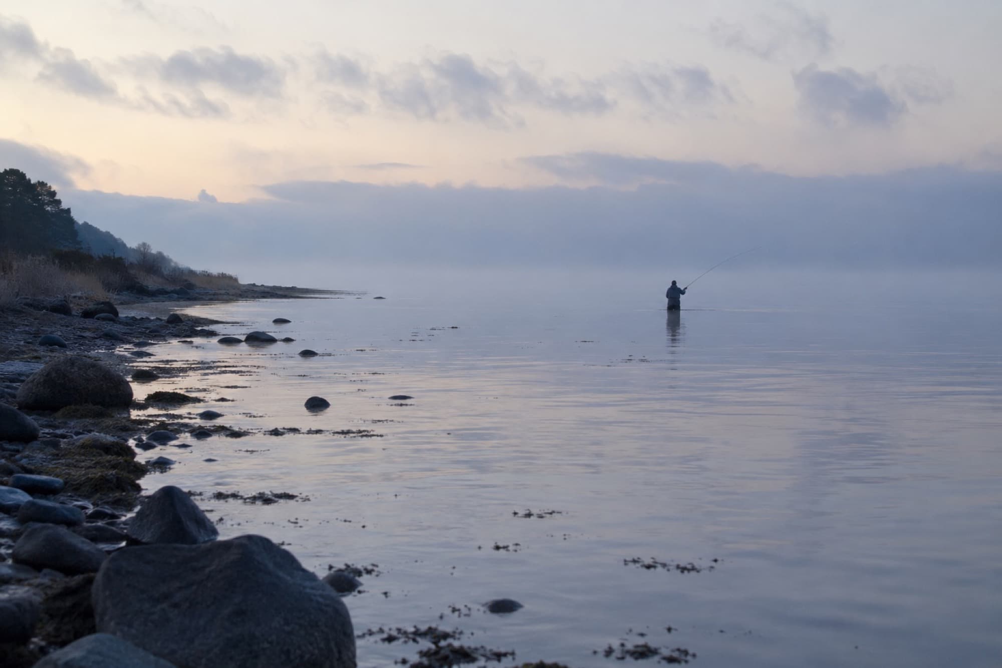 Lystfisker vader stille i havet i tåget morgenlys ved solopgang