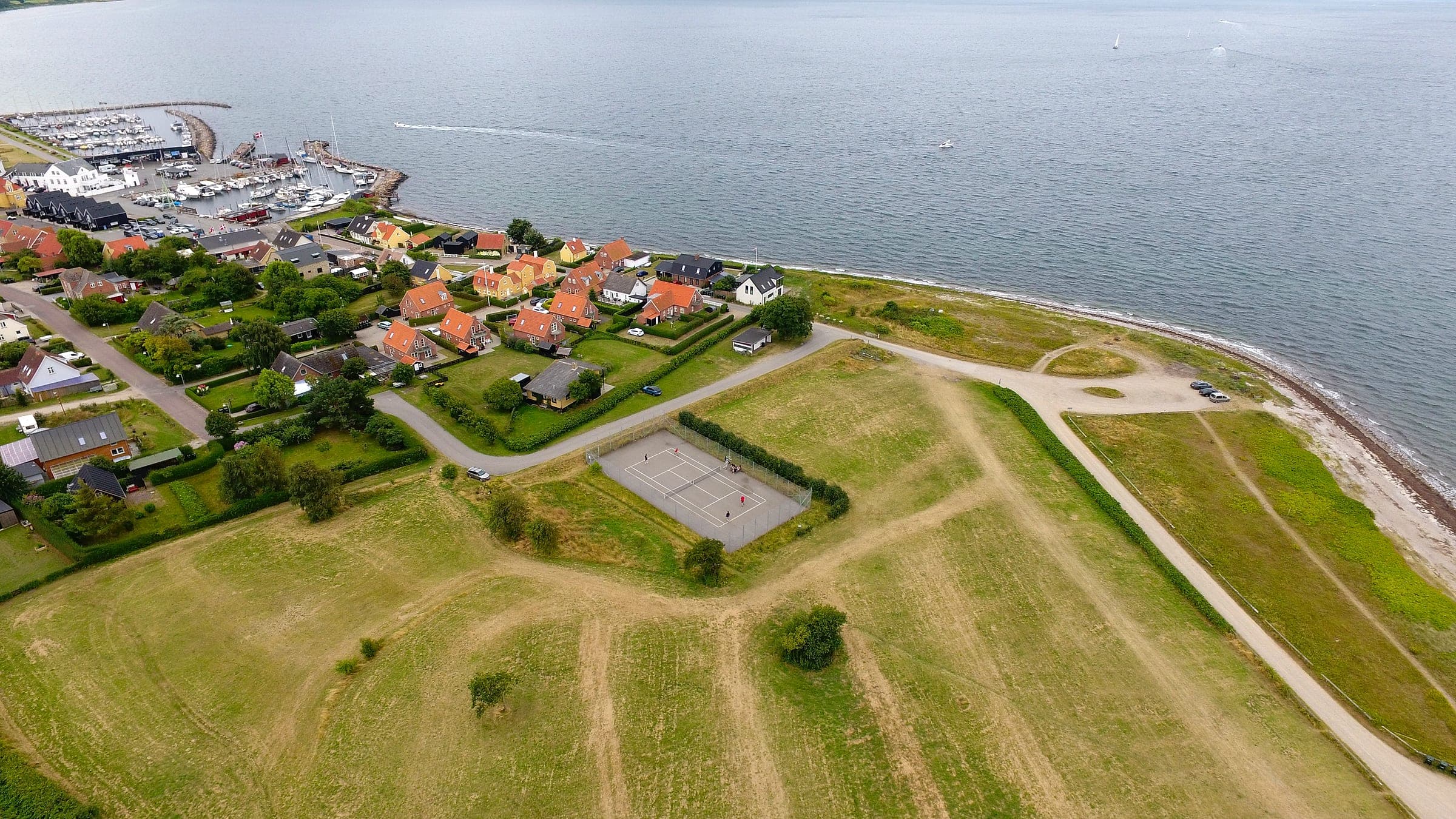 Tennisbanen set fra luften med havnen og sejlbåde i baggrunden